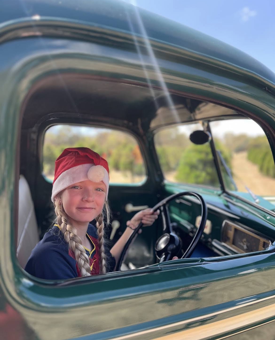 Child in Santa hat sitting in a vintage truck at the farm